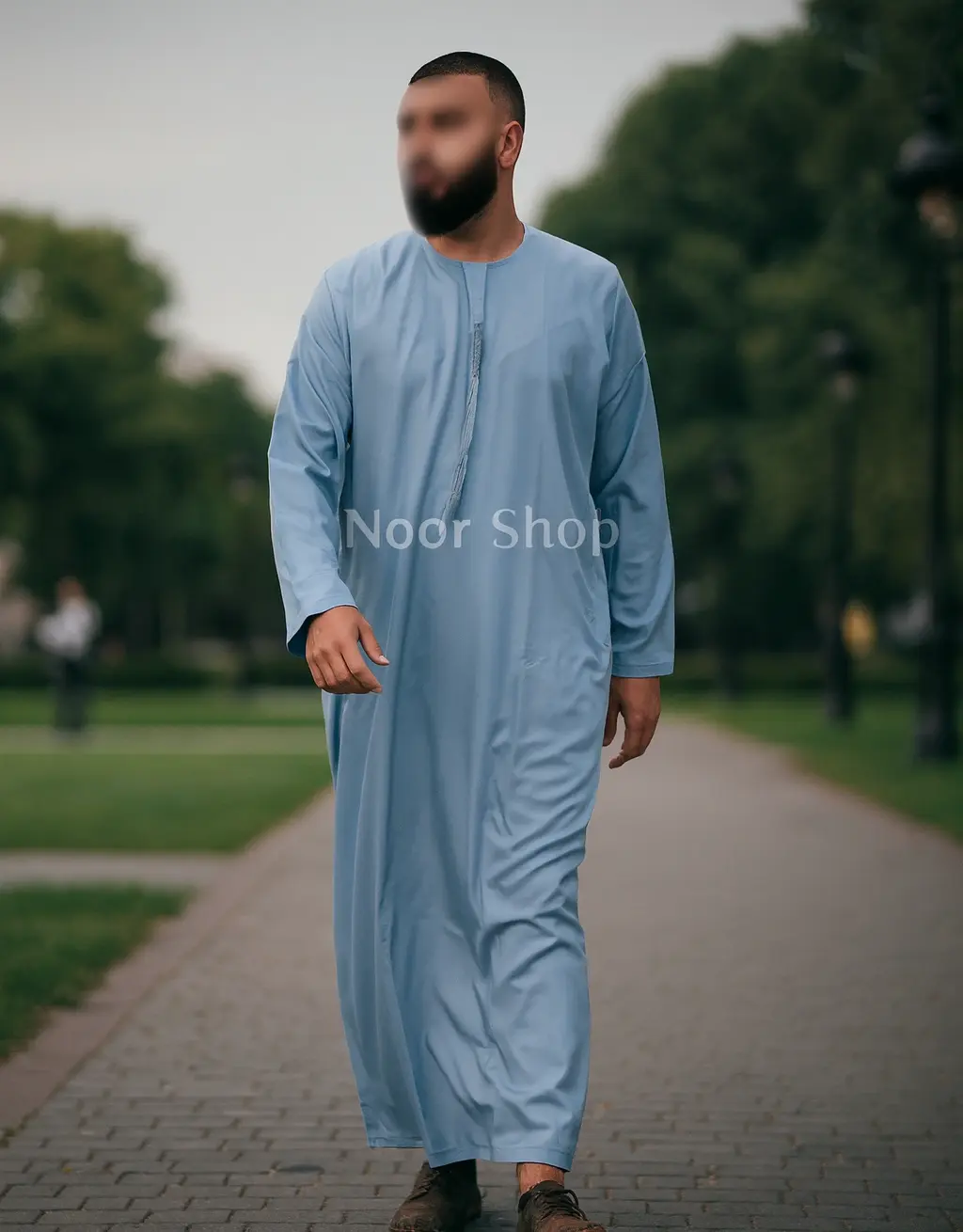 Mann trägt hellblauen Herren Thobe mit dezentem Ausschnitt von Noor Shop und läuft auf einem Weg im Park