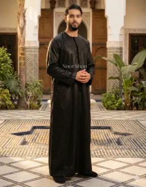Muslimischer Mann trägt schwarzen glänzenden Thobe im marokkanischen Innenhof – Noor Shop