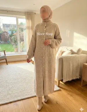 Muslima mit beigem Hijab trägt langes beigefarbenes Strickkleid mit Knopfleiste von Noor Shop in einem hellen Wohnzimmer