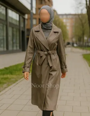 Muslima mit grauem Hijab trägt taupefarbenen Trenchcoat mit Bindegürtel von Noor Shop auf dem Gehweg in der Stadt